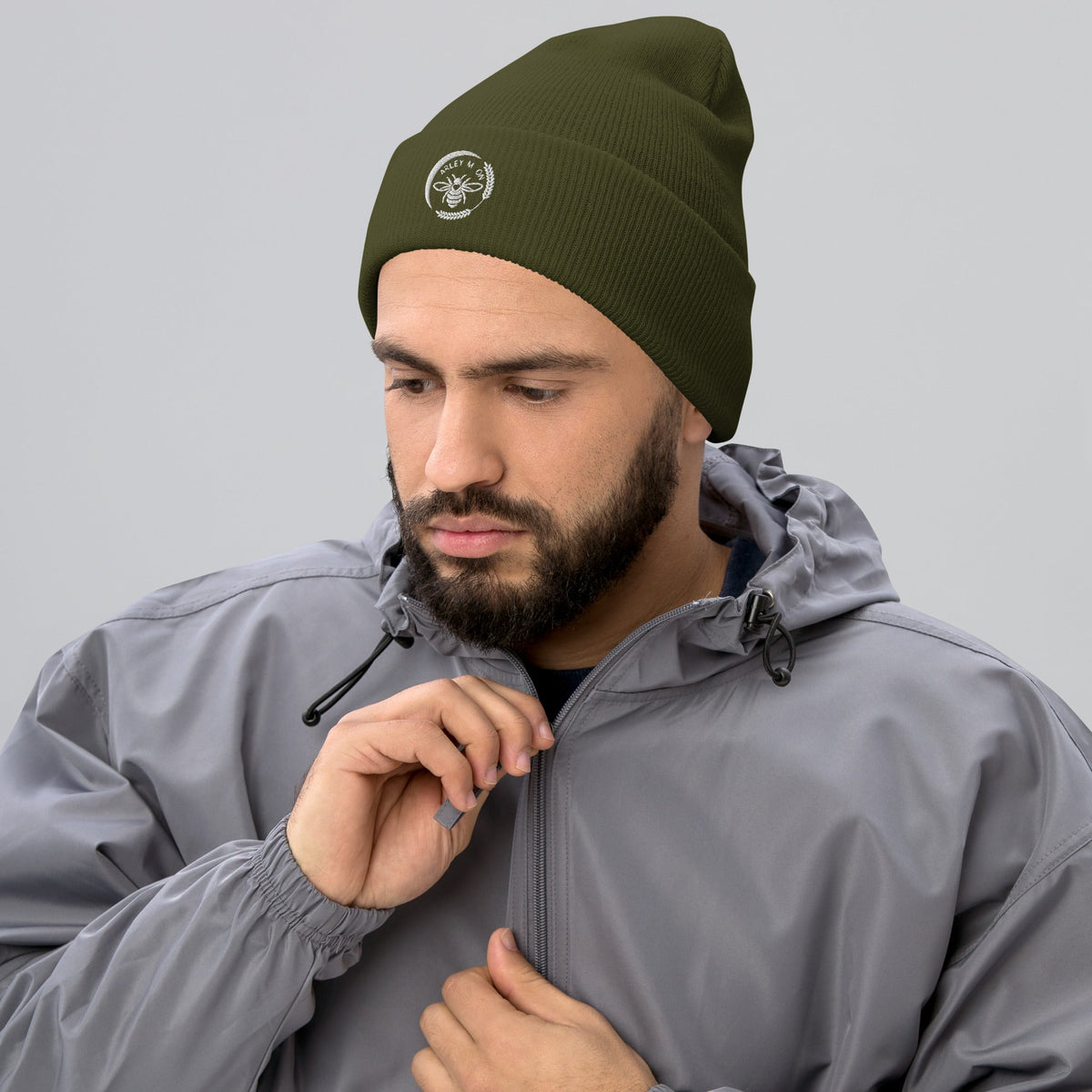 A man wearing a Barley Moon Botanicals olive green cuffed beanie with a white bee and moon logo on the front.