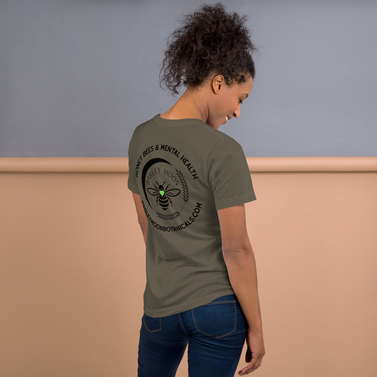 Woman wearing a Barley Moon Botanicals olive green t-shirt with a black bee and crescent moon logo on the back
