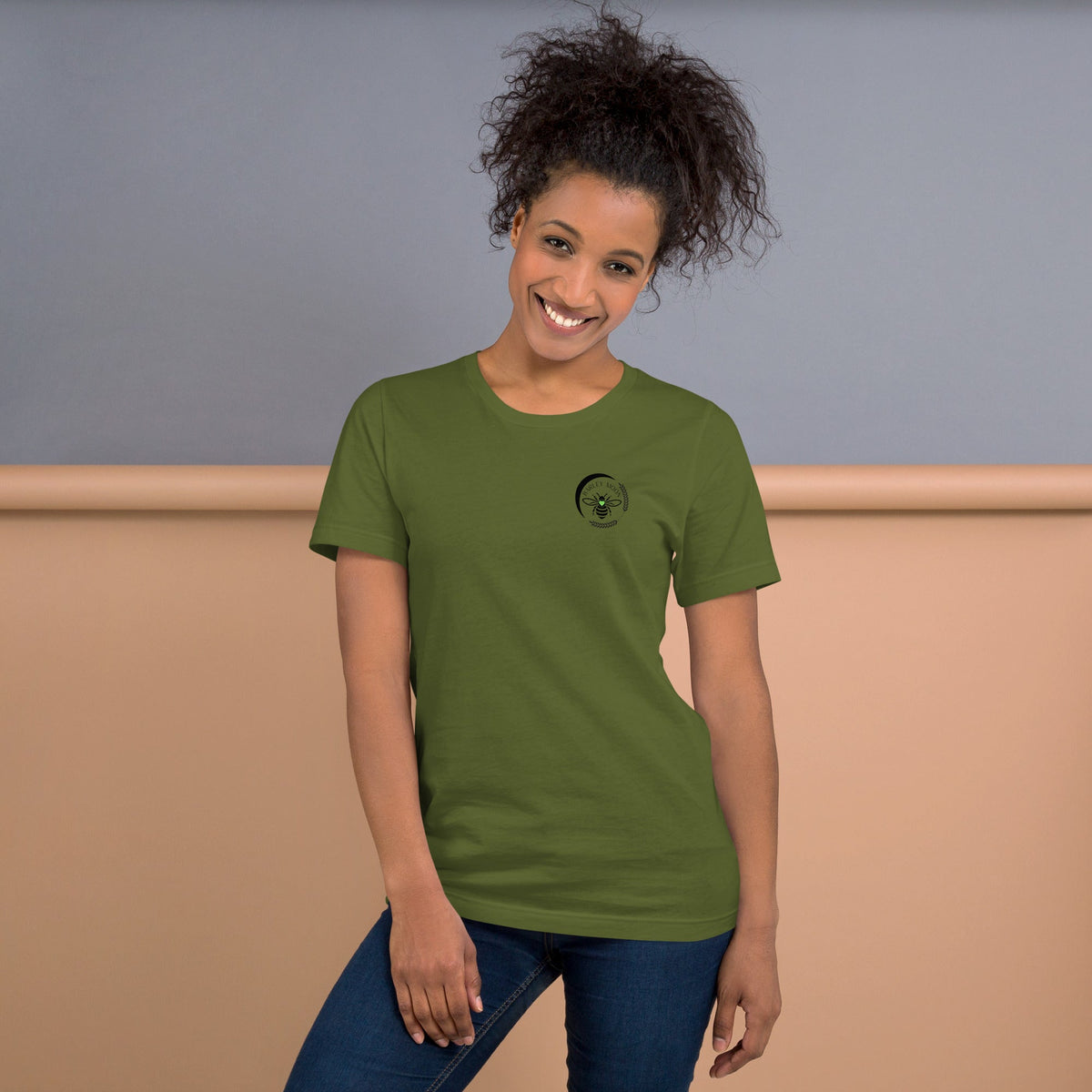 A woman wearing a Barley Moon Botanicals olive green cotton t-shirt with a black bee and crescent moon logo.