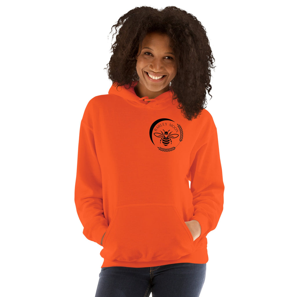 A smiling woman wearing a bright orange Barley Moon Botanicals unisex hoodie with a black bee and moon logo.