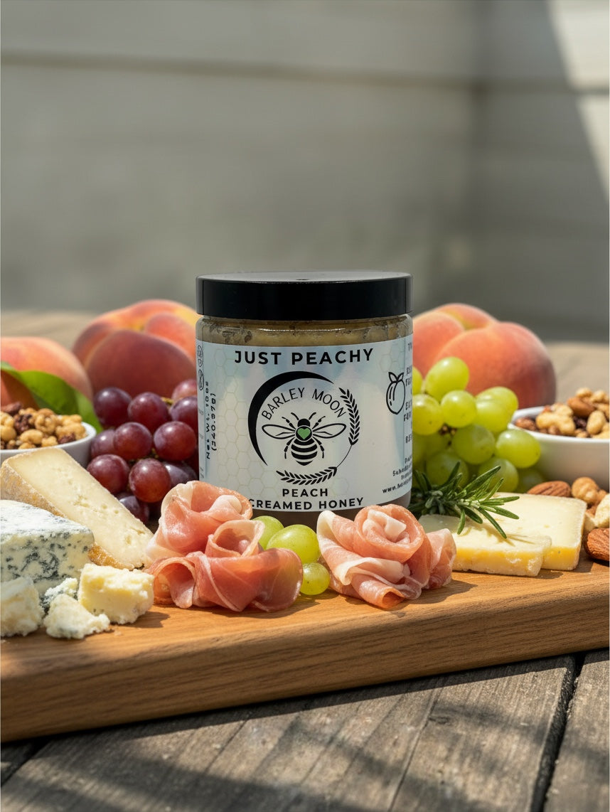 Barley Moon Botanicals Just Peachy creamed honey jar on a charcuterie board with fresh peaches, grapes, and meats.