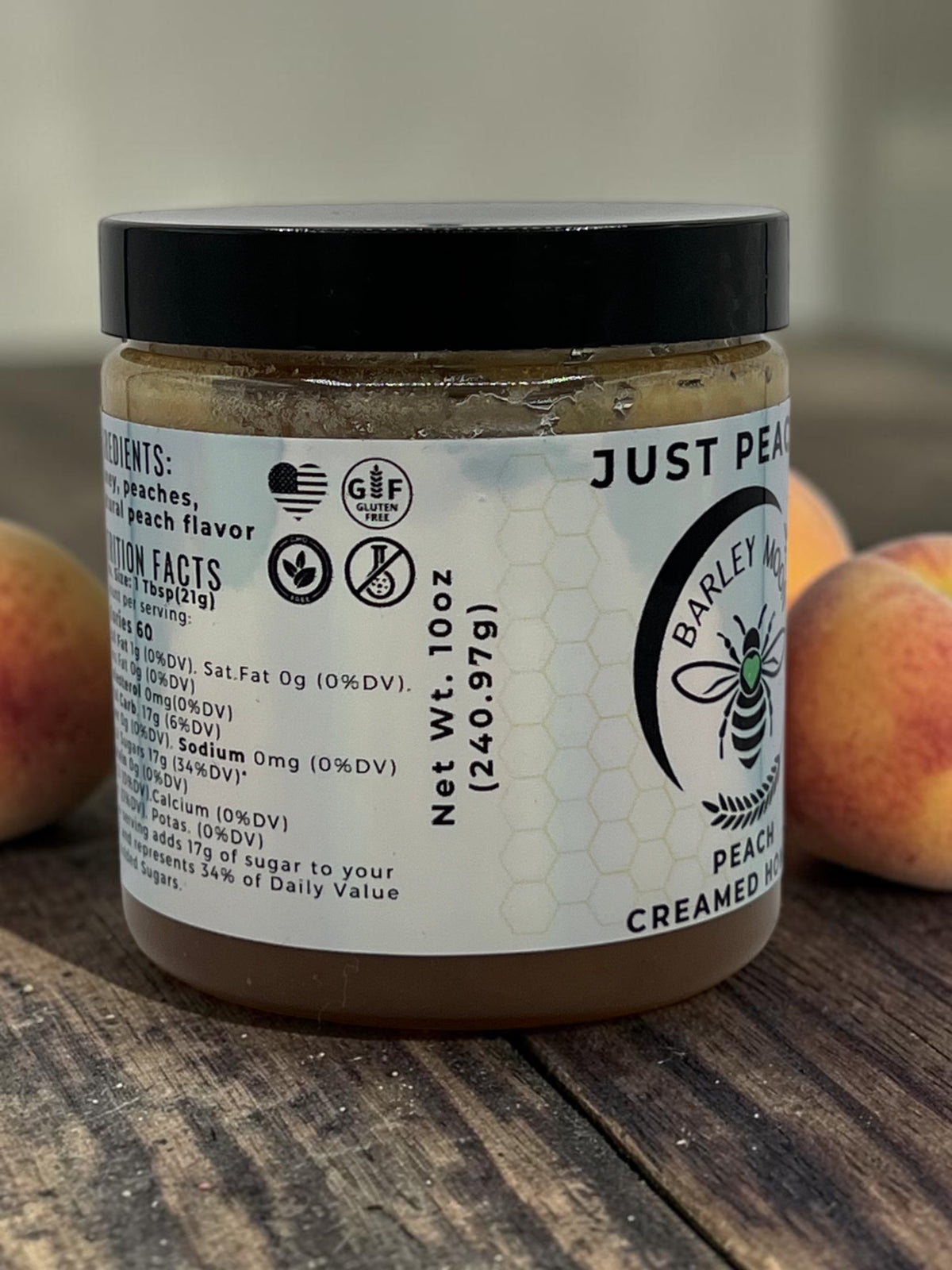 Barley Moon Botanicals Just Peachy creamed honey jar on a wooden surface with fresh peaches in the background.