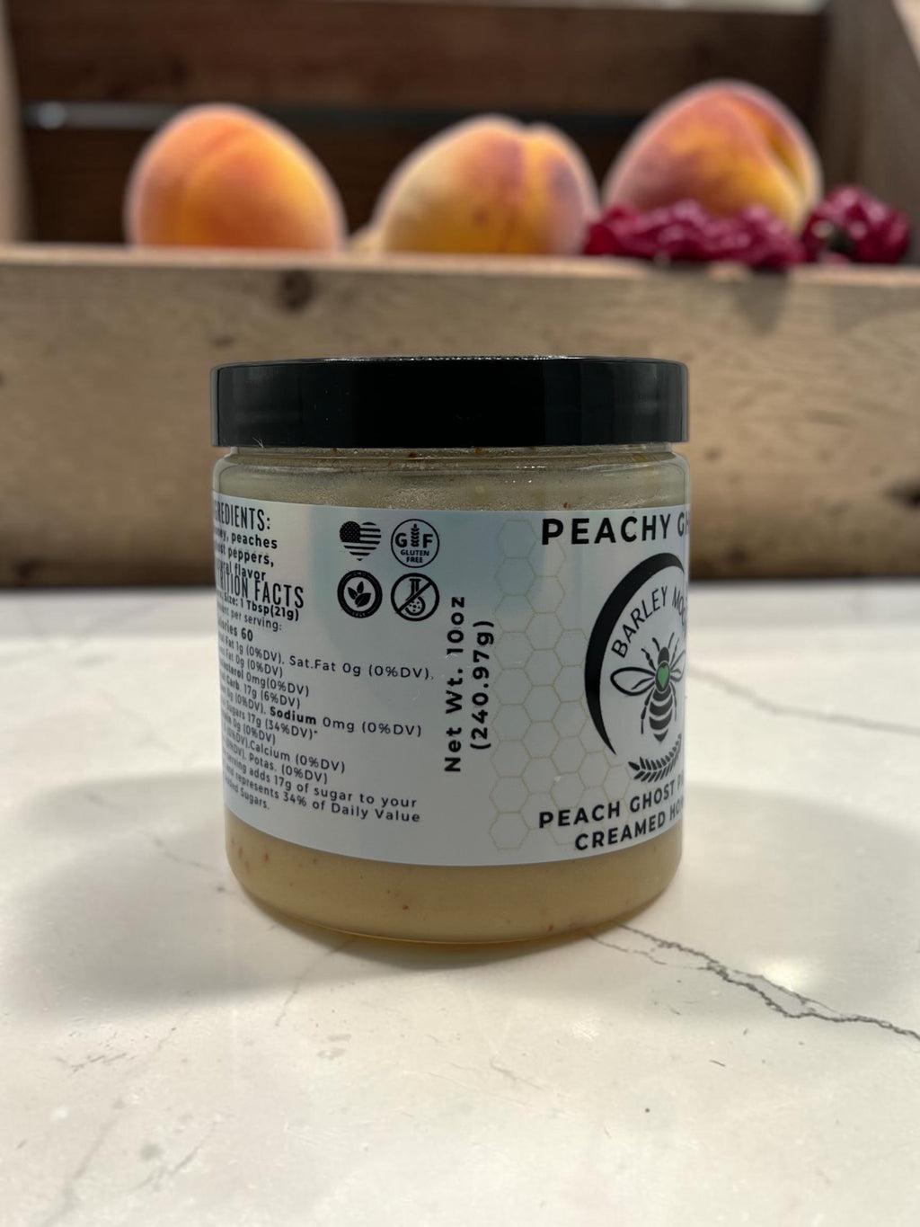 Barley Moon Botanicals Peachy Ghost creamed honey jar with peach and ghost peppers on a white marble surface