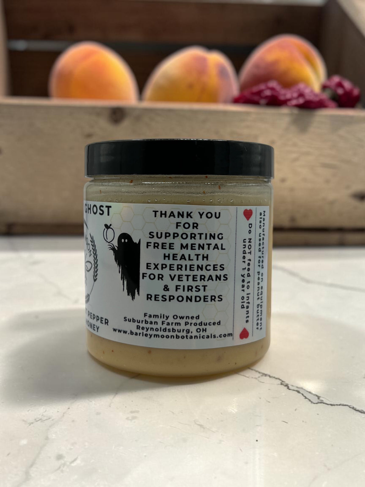 Barley Moon Botanicals Peachy Ghost creamed honey jar with ghost pepper and peaches on a white marble surface