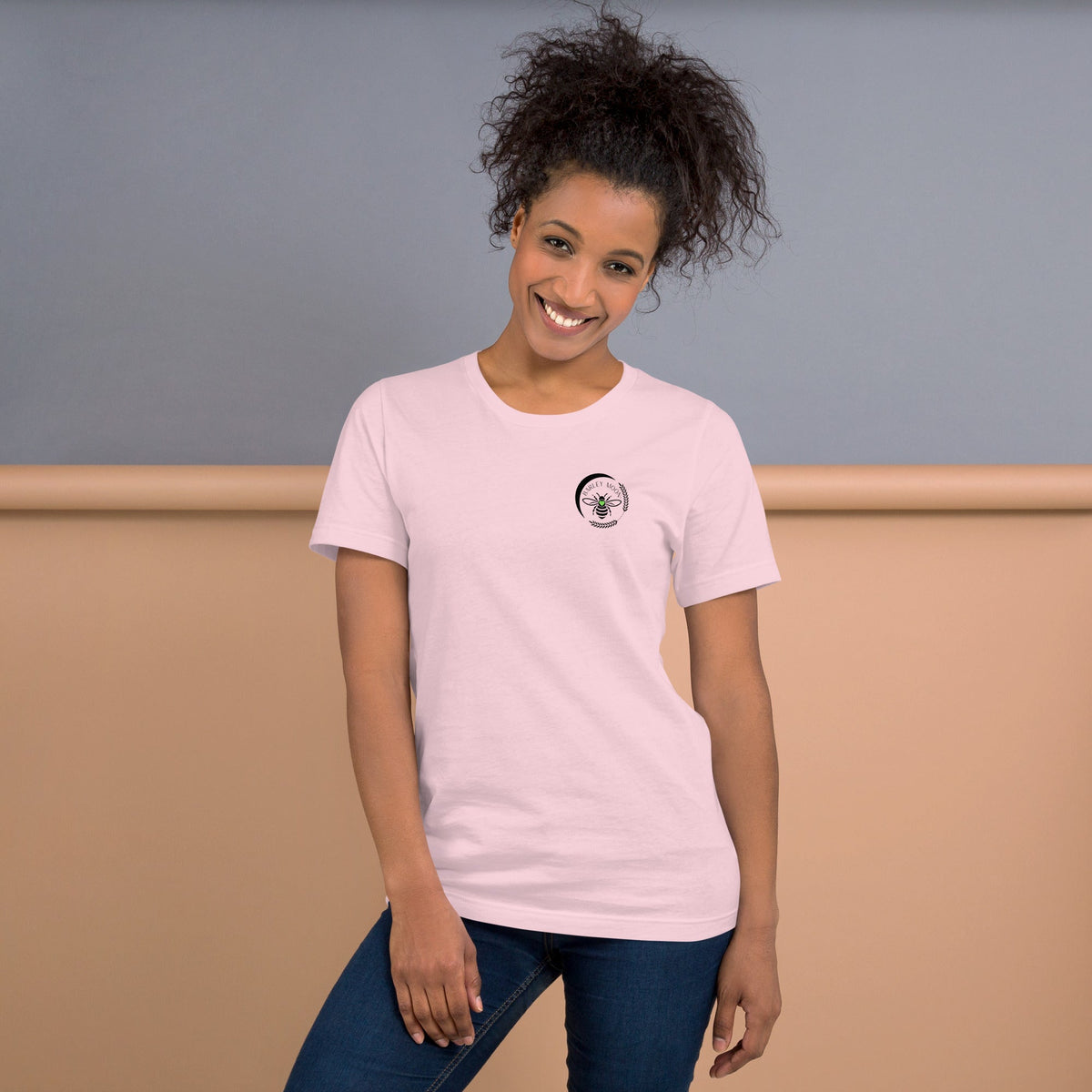 A woman wearing a light pink Barley Moon Botanicals t-shirt with a small black bee and crescent moon logo on the chest.