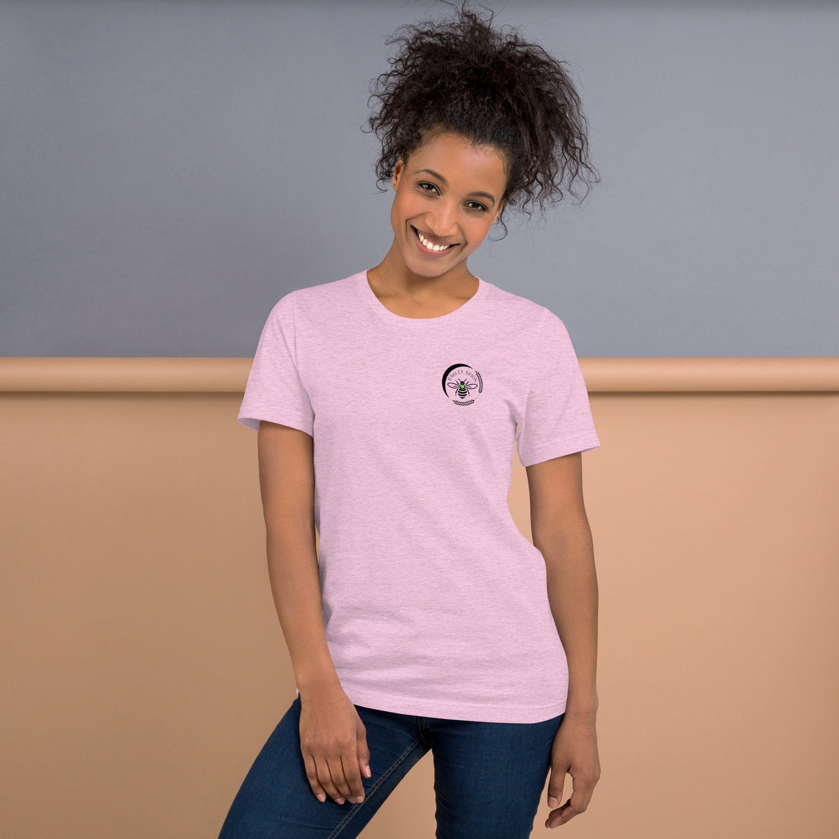 A woman wearing a light pink Barley Moon Botanicals t-shirt with a black bee and crescent moon logo on the chest.