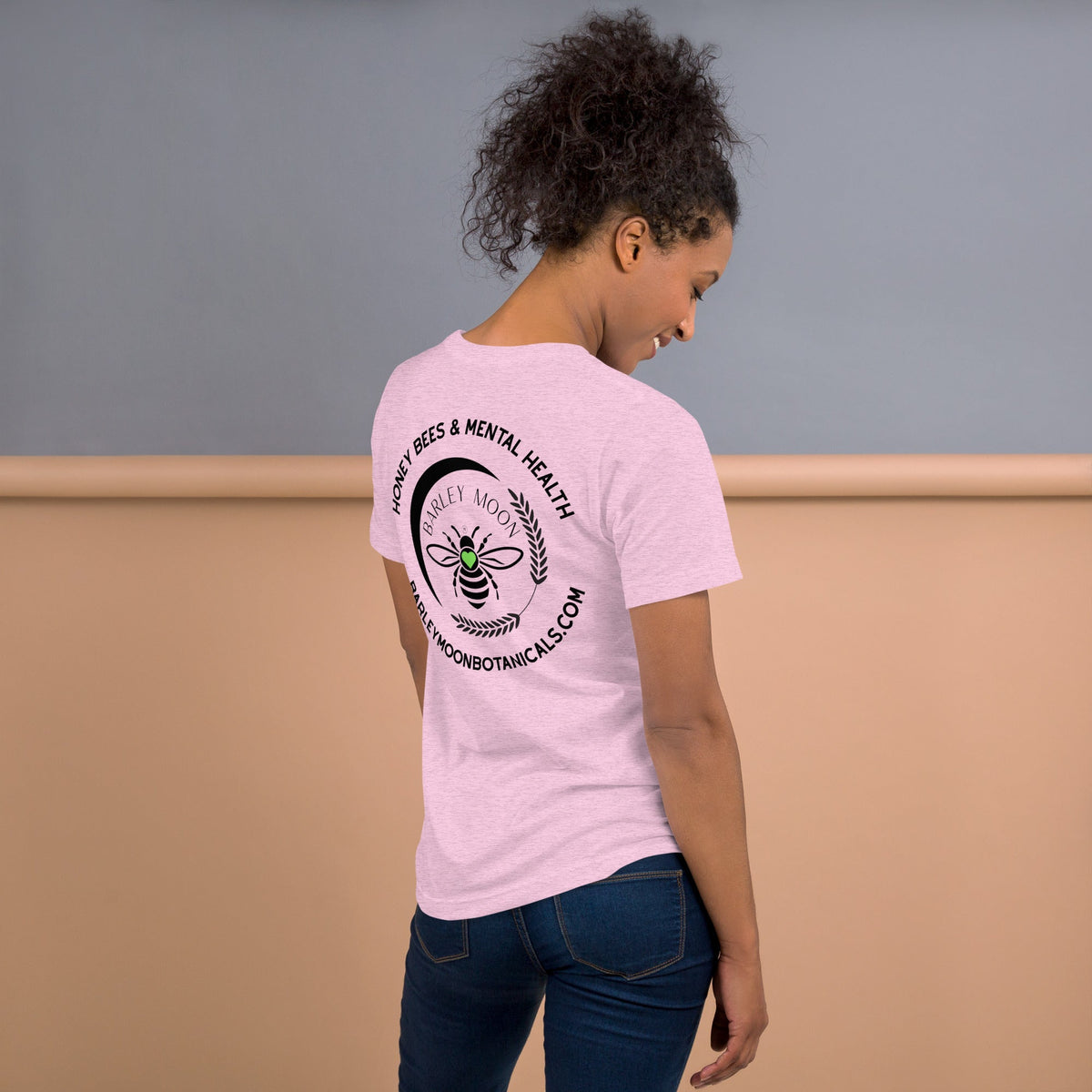 Woman wearing a light pink Barley Moon Botanicals t-shirt with a black bee and crescent moon logo on the back