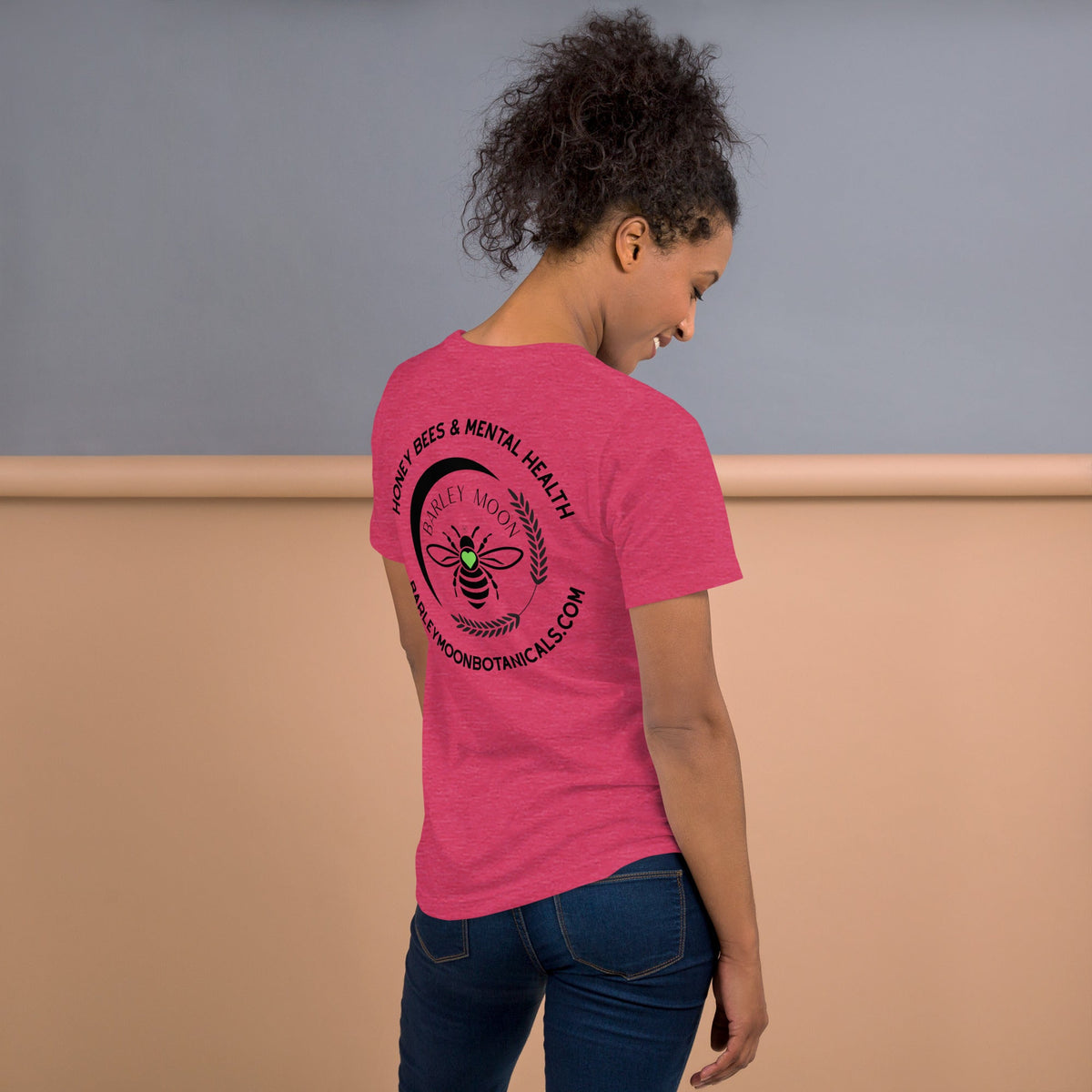 Woman wearing a pink Barley Moon Botanicals t-shirt with a black bee and crescent moon logo on the back