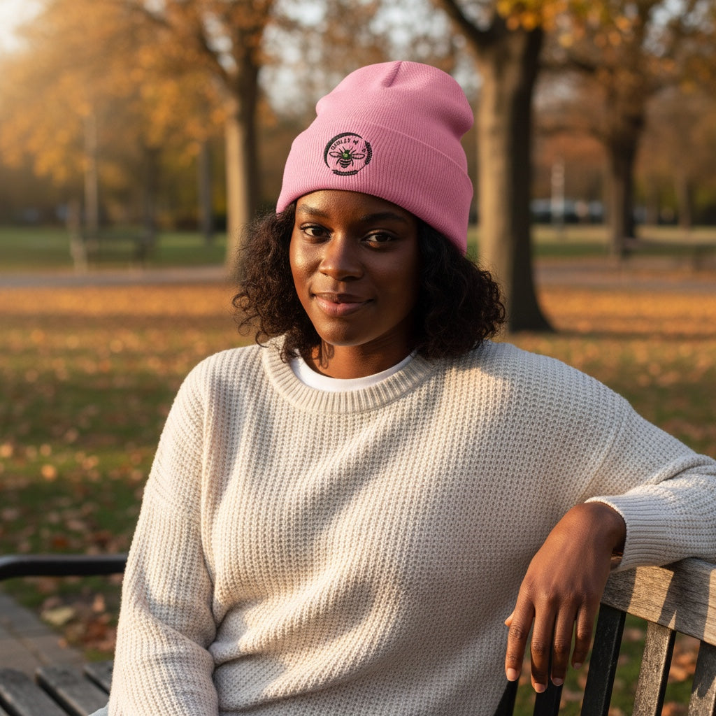 Barley Moon Botanicals pink cuffed beanie with bee and moon logo worn by a woman sitting on a park bench in autumn