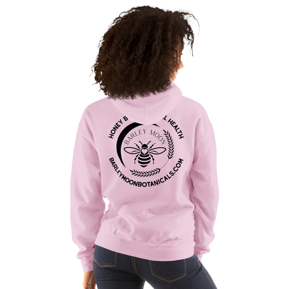 A person wearing a light pink Barley Moon Botanicals unisex hoodie with a black bee and crescent moon logo on the back.