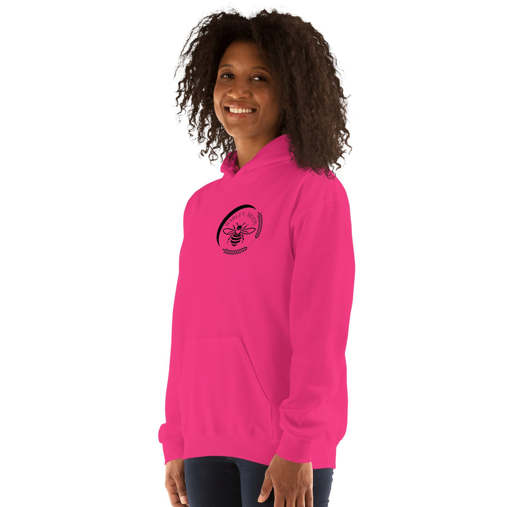 A woman wearing a bright pink Barley Moon Botanicals unisex hoodie with a black bee and crescent moon logo on the chest.