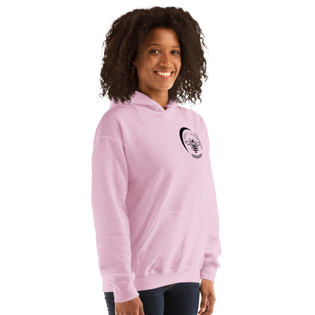 Woman wearing a light pink Barley Moon Botanicals unisex hoodie with a black bee and crescent moon logo on the chest.