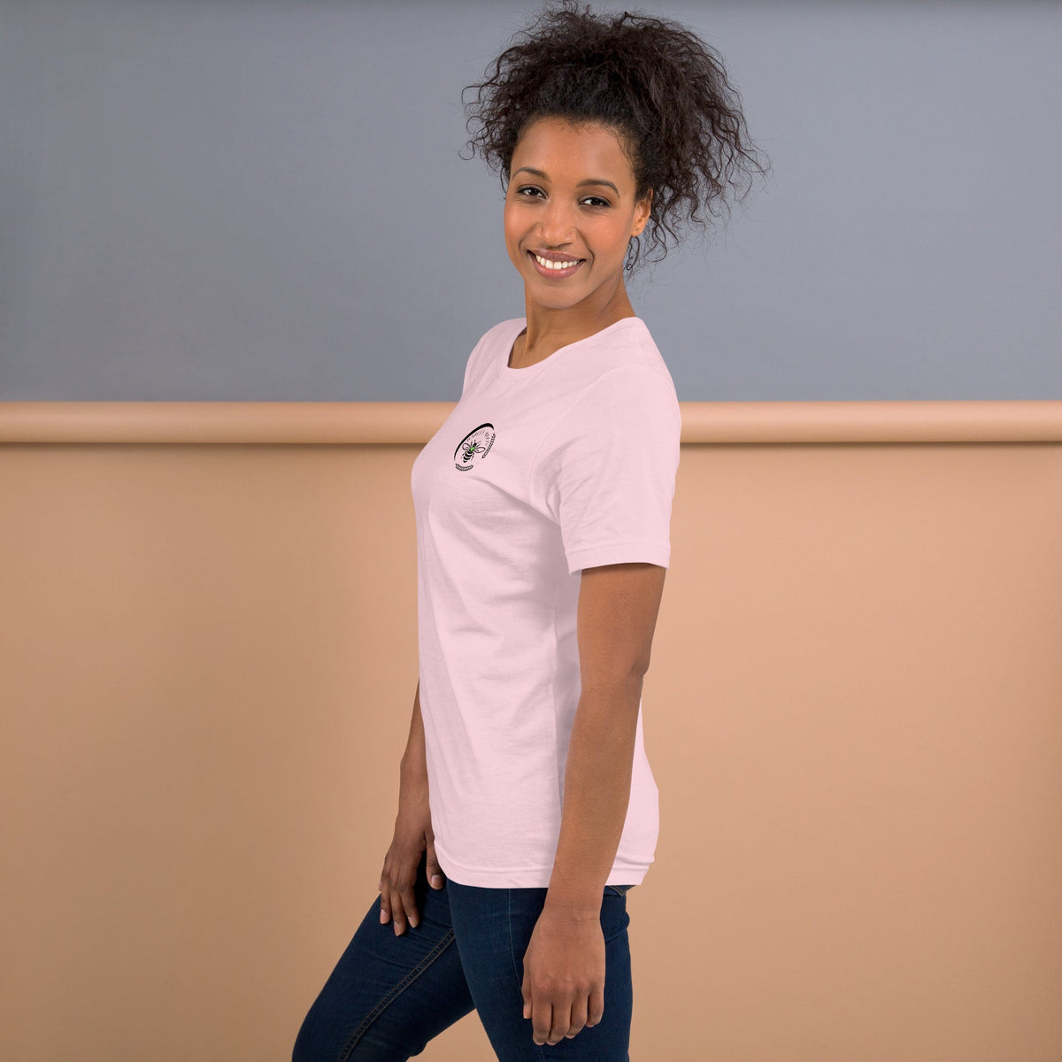 A woman wearing a light pink Barley Moon Botanicals t-shirt with a small bee and crescent moon logo on the chest.