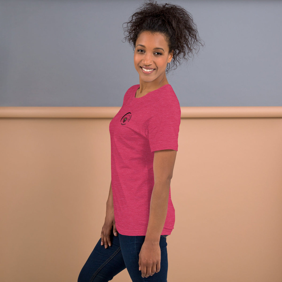 A woman wearing a pink Barley Moon Botanicals t-shirt with a small black bee and crescent moon logo on the chest.