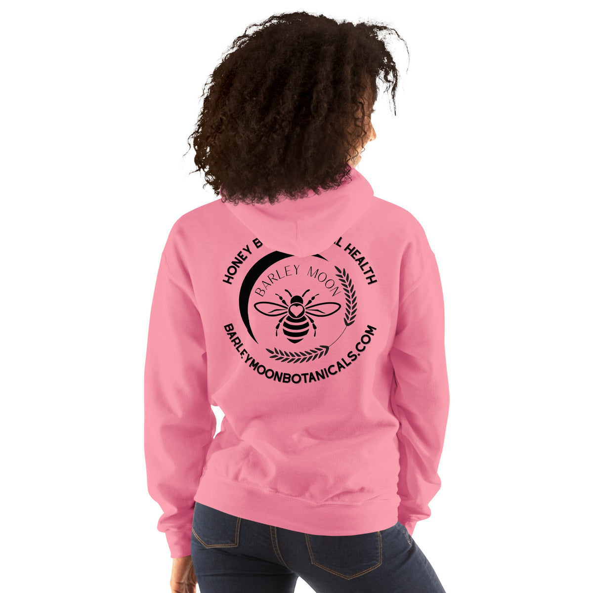 A person wearing a pink Barley Moon Botanicals unisex hoodie with a black bee and crescent moon logo on the back.