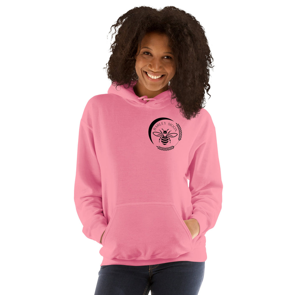 A smiling woman wearing a pink Barley Moon Botanicals unisex hoodie with a black bee and crescent moon logo.
