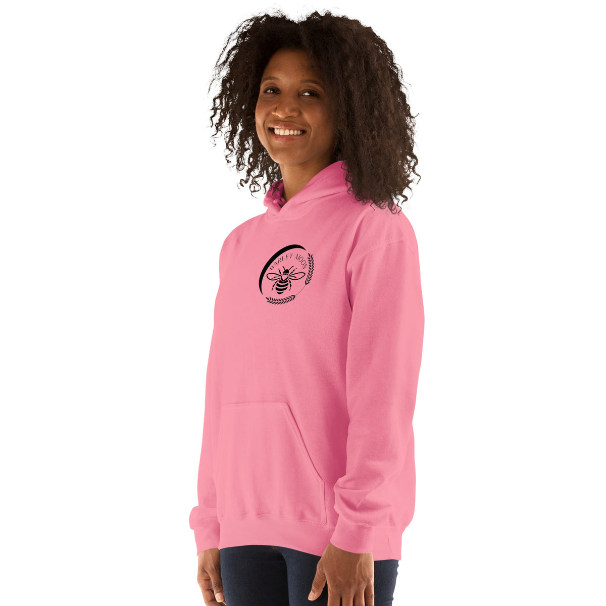 A woman wearing a pink Barley Moon Botanicals unisex hoodie with a black bee and crescent moon logo on the chest.