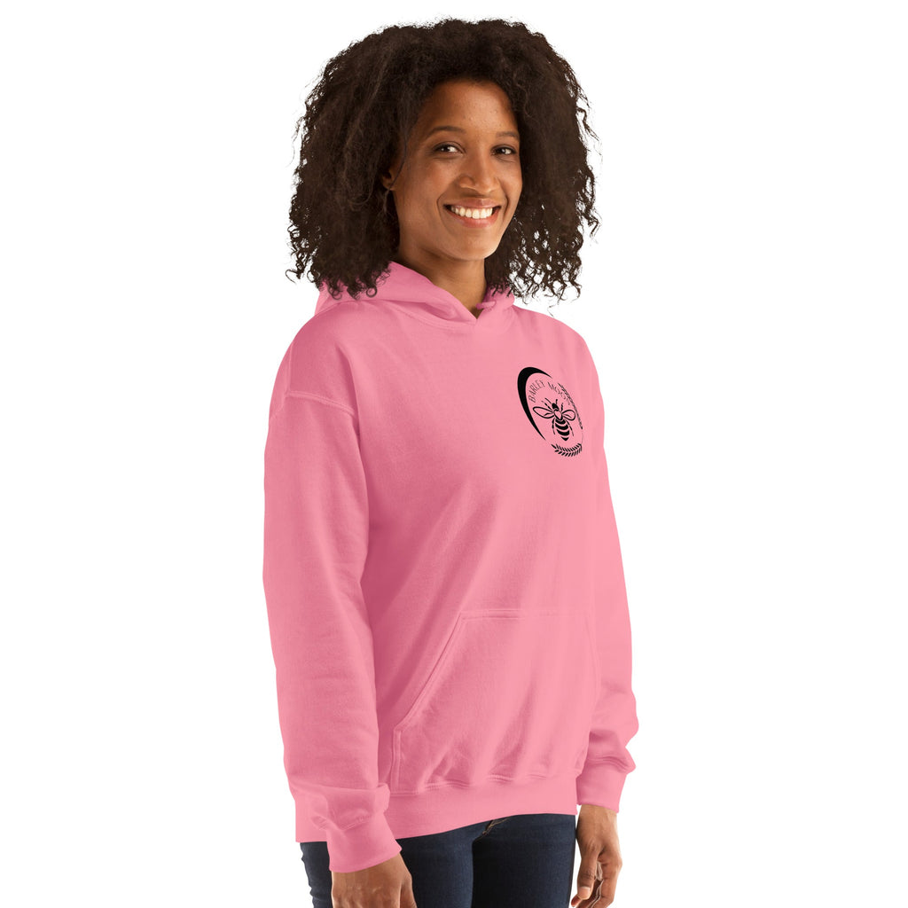A woman wearing a pink Barley Moon Botanicals unisex hoodie featuring a black bee and crescent moon logo on the chest.