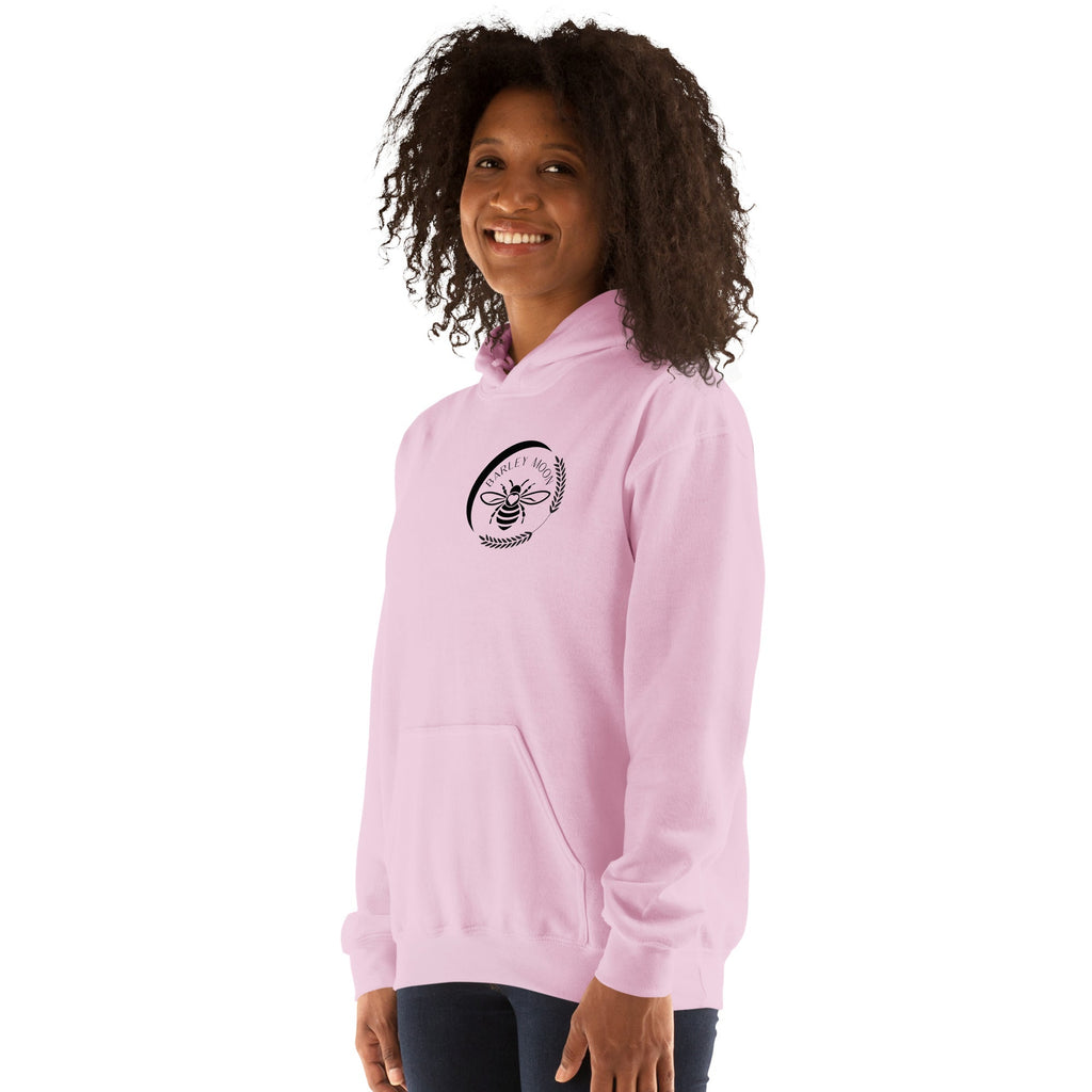 Woman wearing a light pink Barley Moon Botanicals unisex hoodie with a black bee and crescent moon logo on the chest.