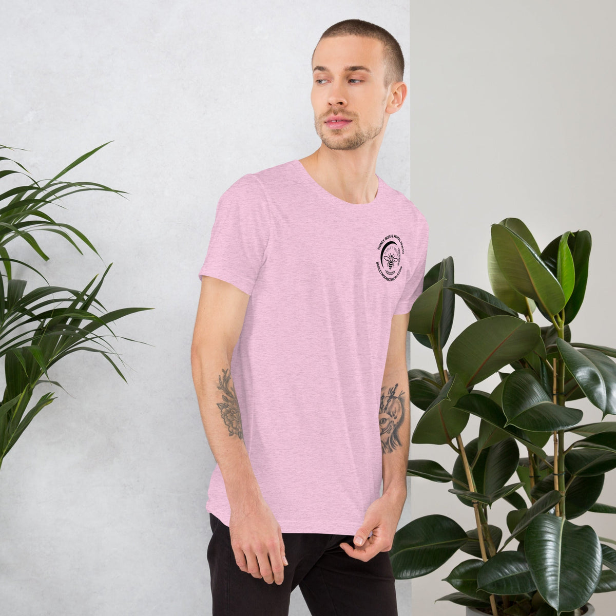 A man wearing a light pink Barley Moon Botanicals unisex t-shirt with a small circular bee logo on the chest.