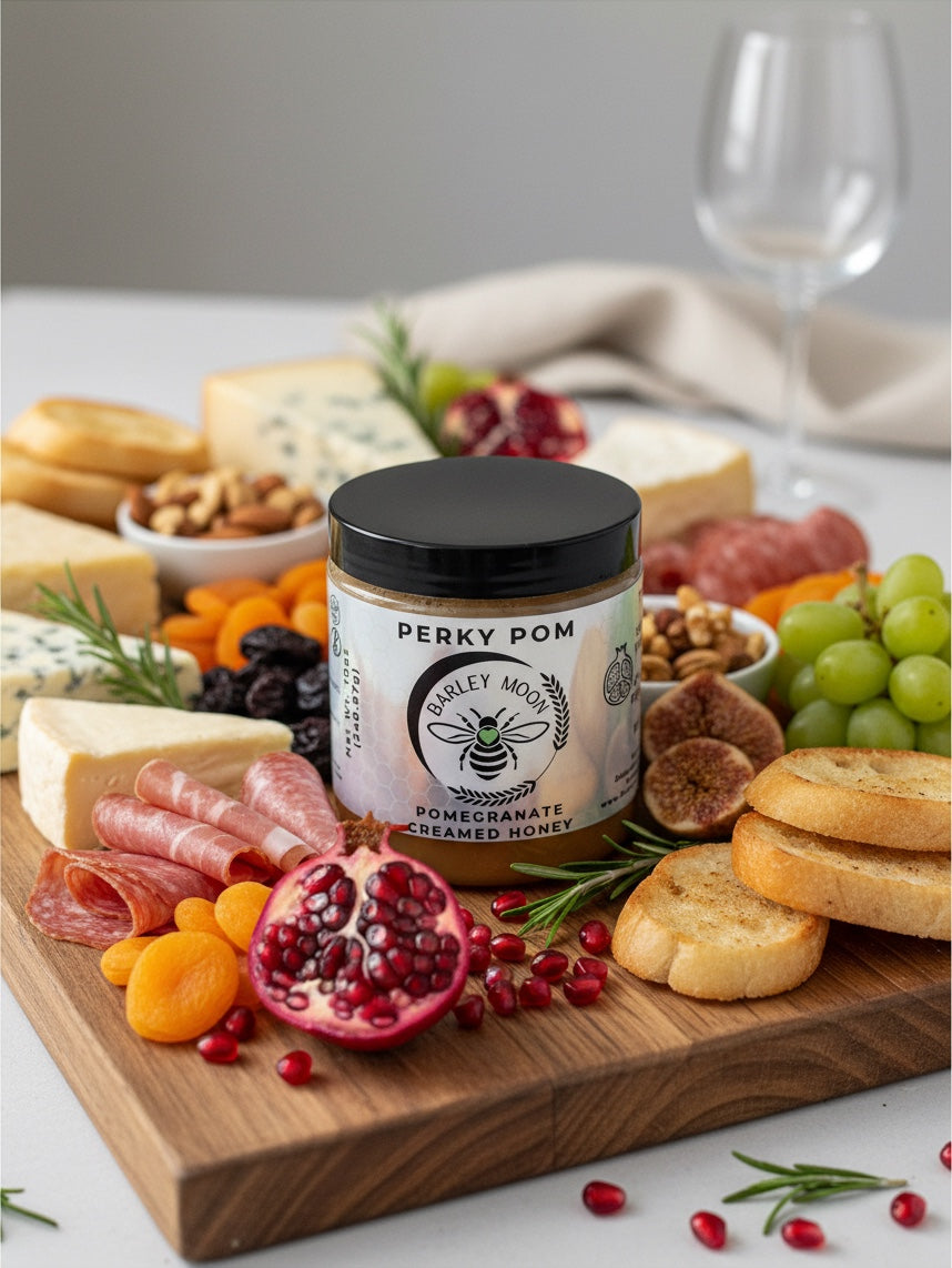 Barley Moon Botanicals Perky Pom pomegranate creamed honey jar centered on a gourmet cheese and charcuterie board.
