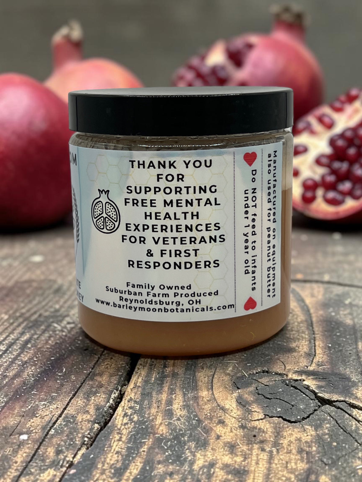 Barley Moon Botanicals Perky Pom pomegranate creamed honey jar on a wooden surface with fresh pomegranates behind.
