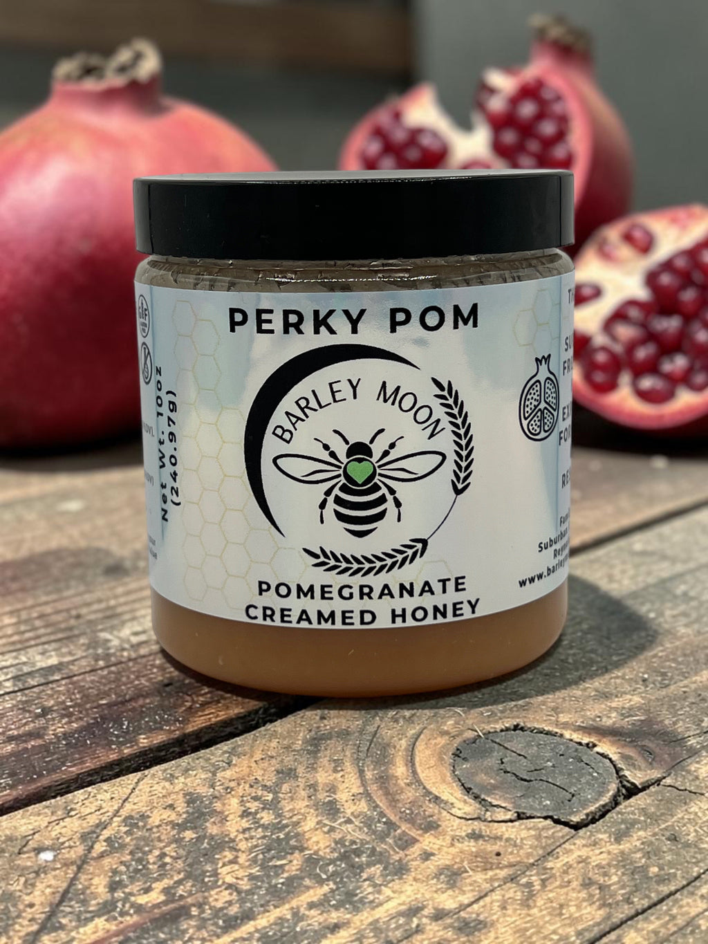 Barley Moon Botanicals Perky Pom pomegranate creamed honey in a glass jar on a wooden surface with fresh pomegranates
