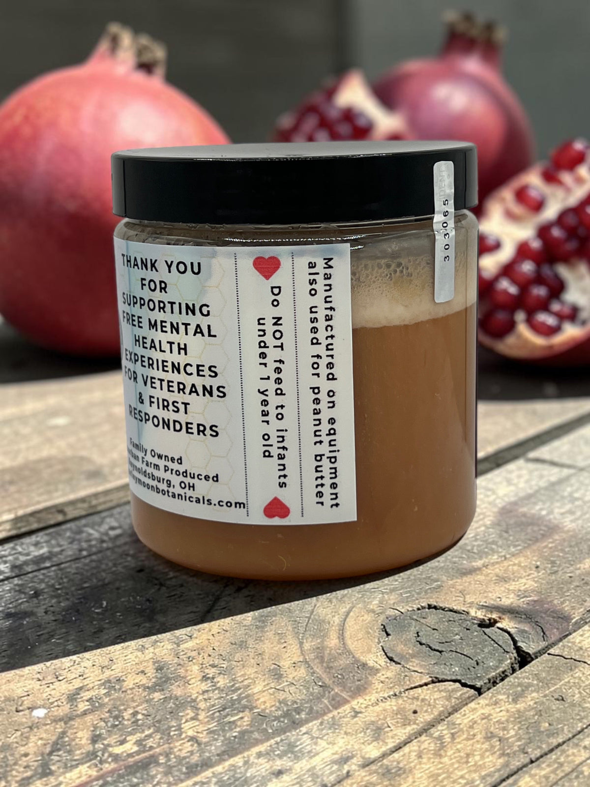 Barley Moon Botanicals Perky Pom pomegranate creamed honey in a glass jar with fresh pomegranates on a wooden table.