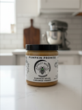 Barley Moon Botanicals Pumpkin Promise creamed honey in a glass jar with a black lid on a white kitchen counter.