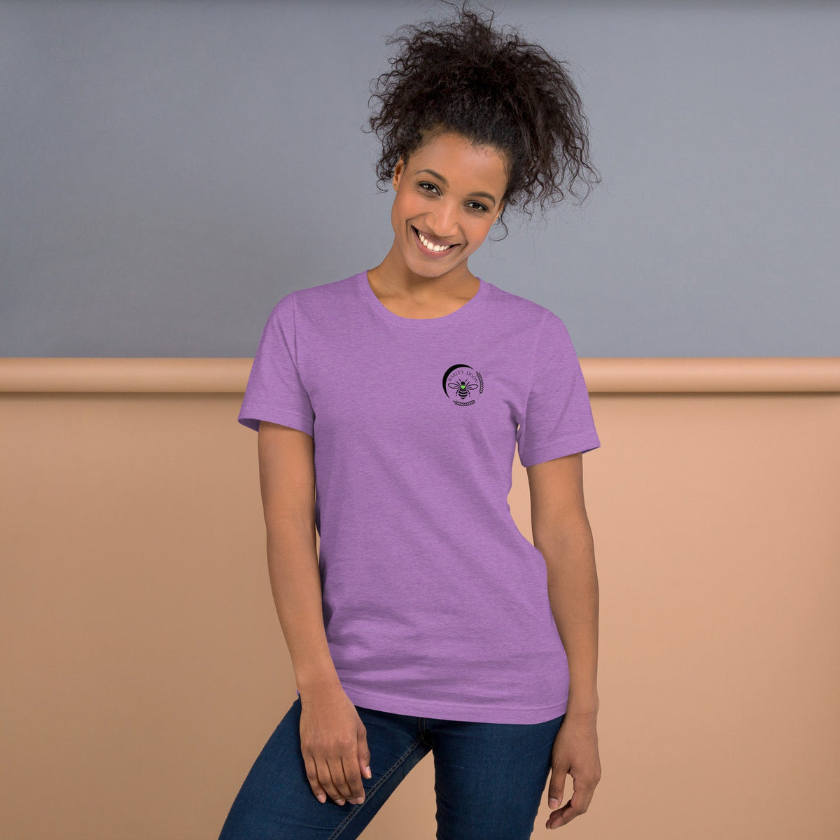 A smiling woman wearing a soft purple Barley Moon Botanicals t-shirt with a black bee and crescent moon logo.