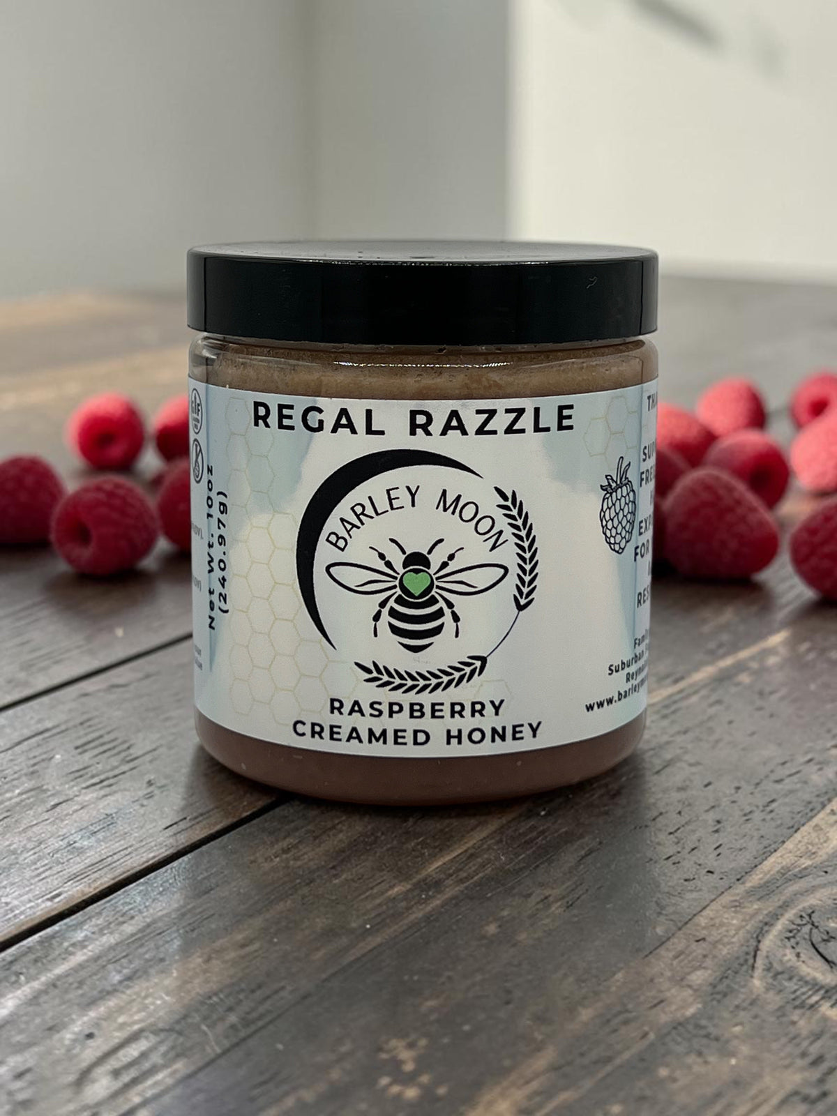 Barley Moon Botanicals Regal Razzle raspberry creamed honey in a glass jar surrounded by fresh raspberries