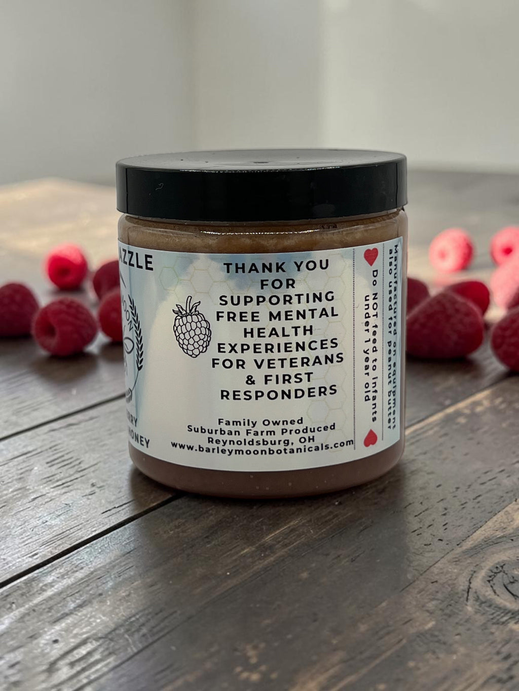 Barley Moon Botanicals Regal Razzle creamed raspberry honey jar on a wooden table surrounded by fresh raspberries