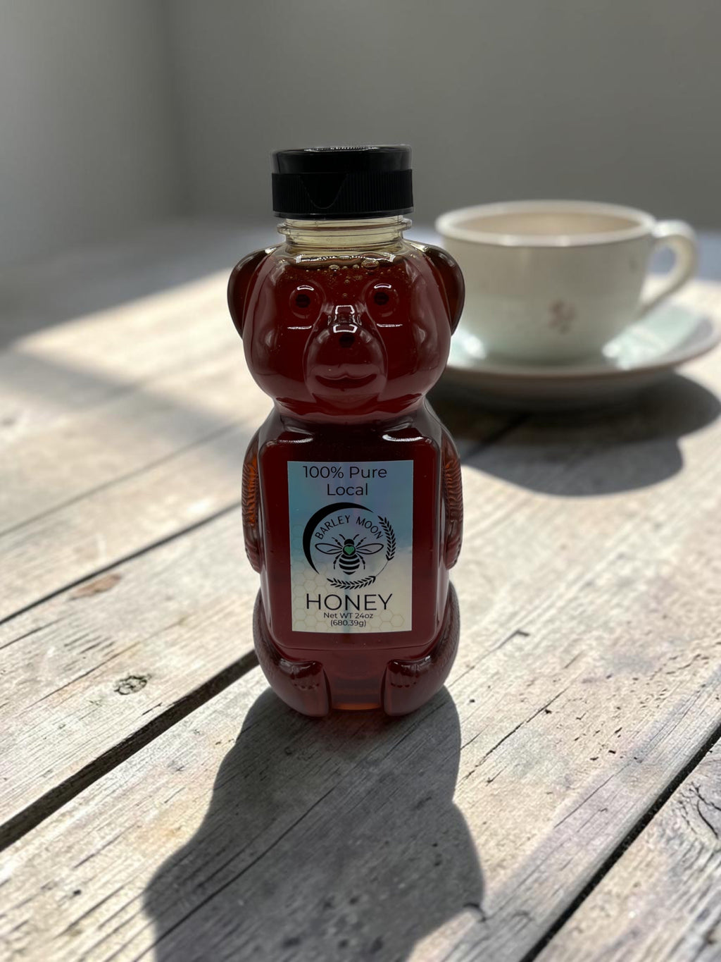 Barley Moon Botanicals raw honey in a bear-shaped bottle on a rustic wooden table with a teacup in the background.