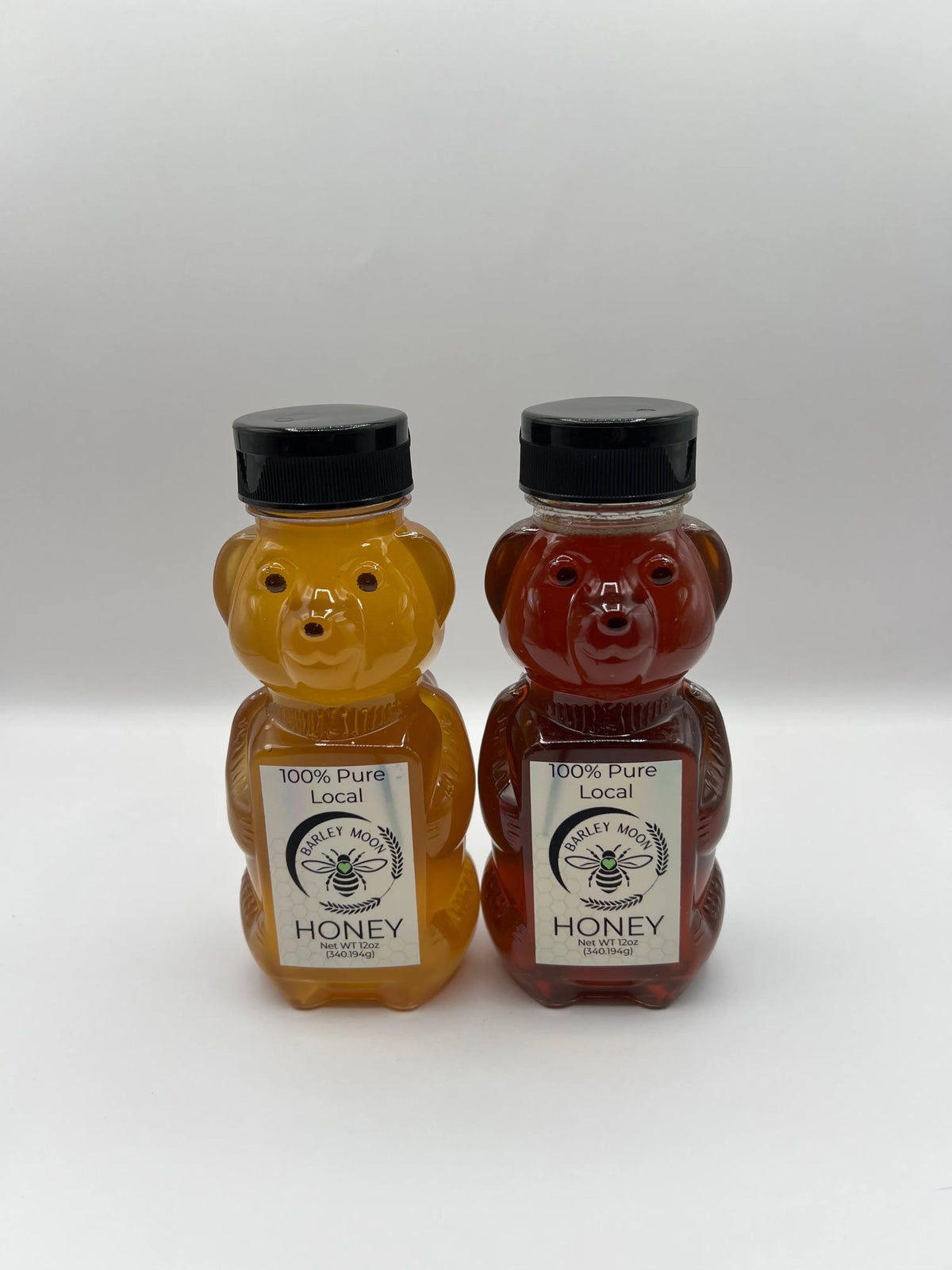 Two Barley Moon Botanicals bear-shaped bottles of raw, unfiltered local honey with black caps on a white background.