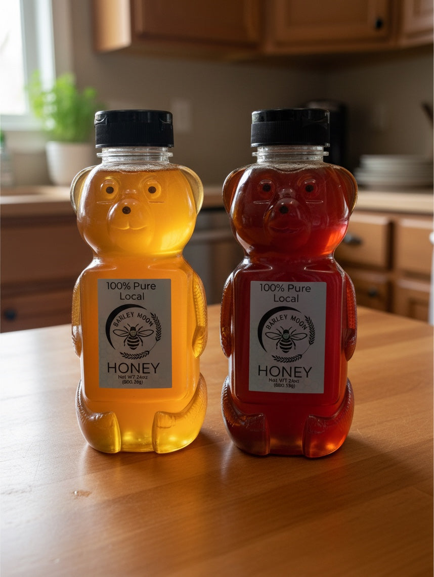 Barley Moon Botanicals raw honey in two bear-shaped bottles with light and dark amber honey on a wooden kitchen table.