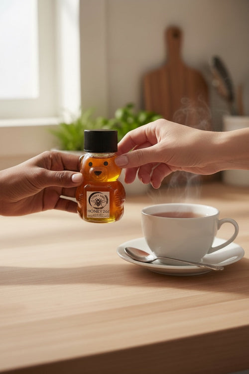 Barley Moon Botanicals 2oz raw honey in a bear-shaped bottle being held over a steaming cup of tea on a wooden table.