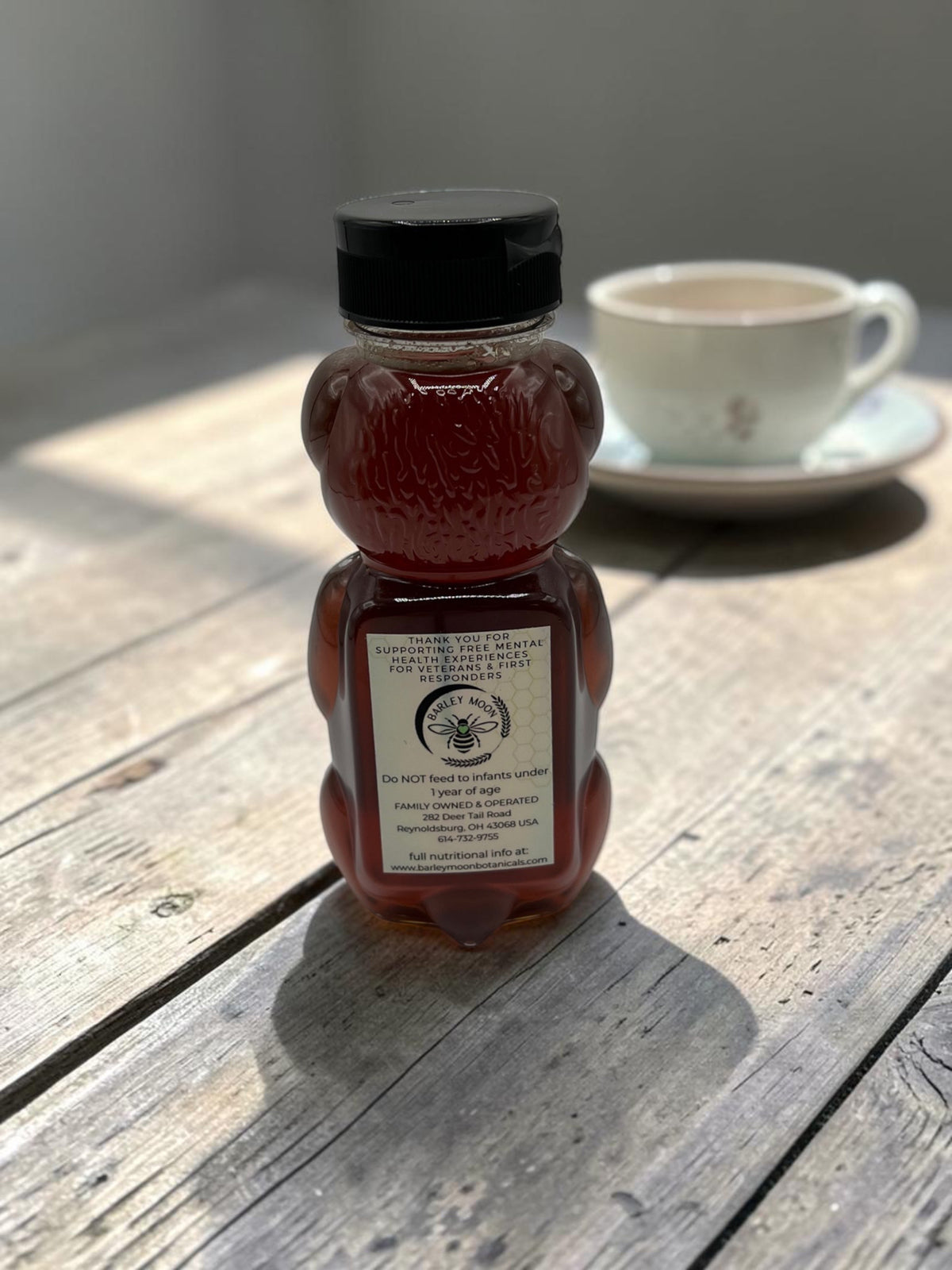 Barley Moon Botanicals pure raw local honey in a classic bear-shaped bottle sitting on a rustic wooden table.