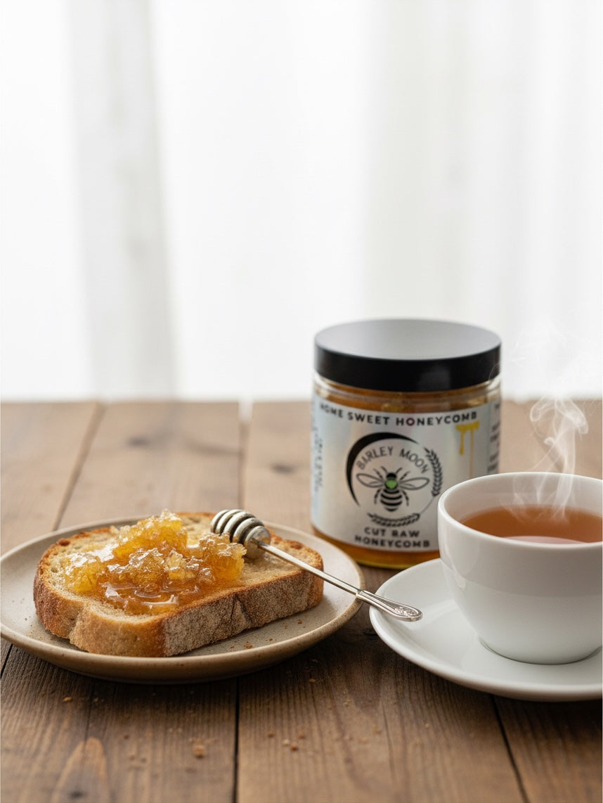 Barley Moon Botanicals raw honeycomb on a slice of toasted bread next to a steaming cup of tea and a honey jar.