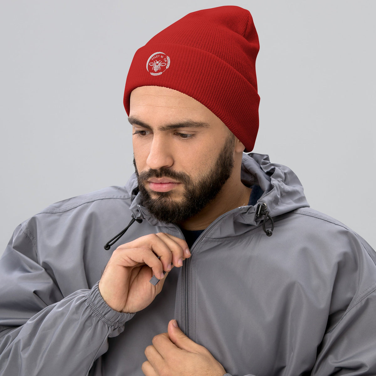 A man wearing a red Barley Moon Botanicals cuffed beanie with a white bee and moon logo, paired with a grey jacket.