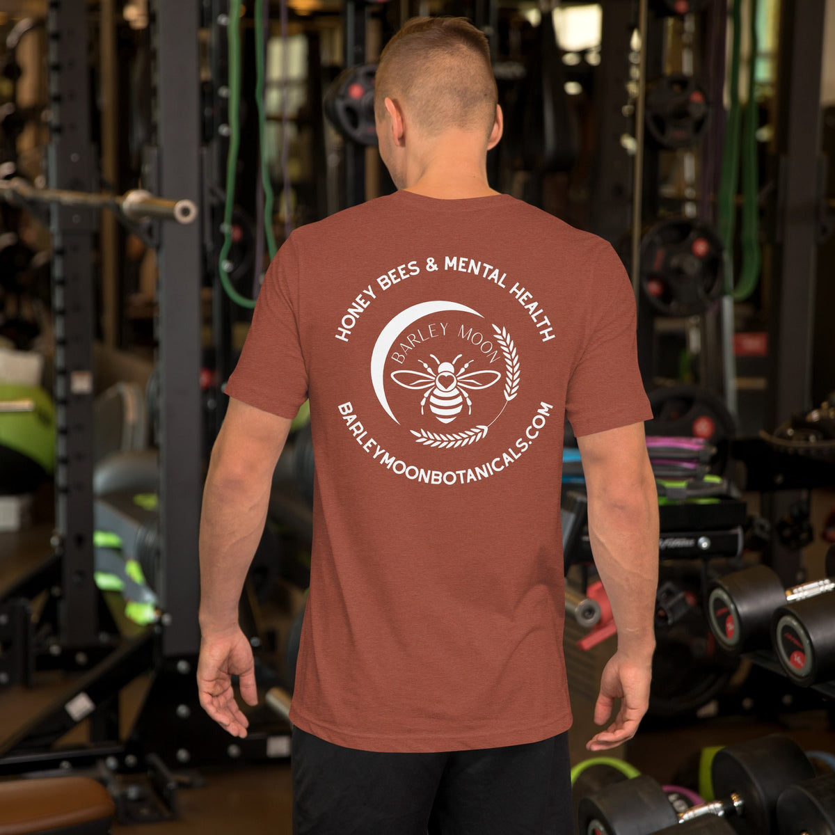 Barley Moon Botanicals rust-colored cotton t-shirt with white bee and moon logo on the back, worn by a man in a gym.