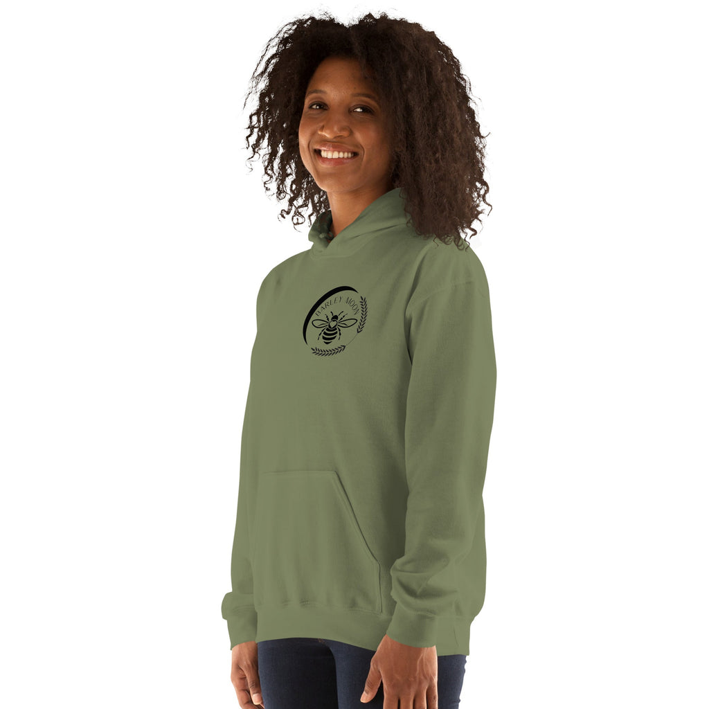 A woman wearing a Barley Moon Botanicals olive green unisex hoodie with a black bee and crescent moon logo on the chest