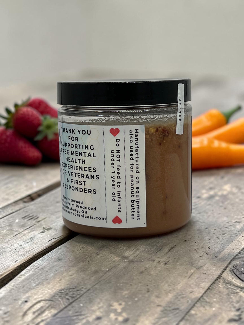 Barley Moon Botanicals Strawbanero creamed honey jar with strawberry and habanero pepper accents on a rustic wood table.