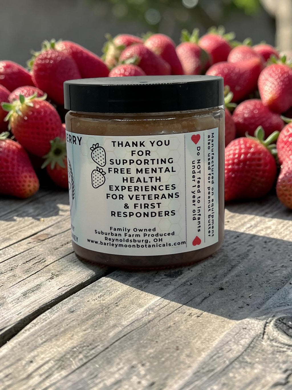 Barley Moon Botanicals Sweetie Berry creamed honey jar with a label about supporting veterans, set against fresh strawberries.