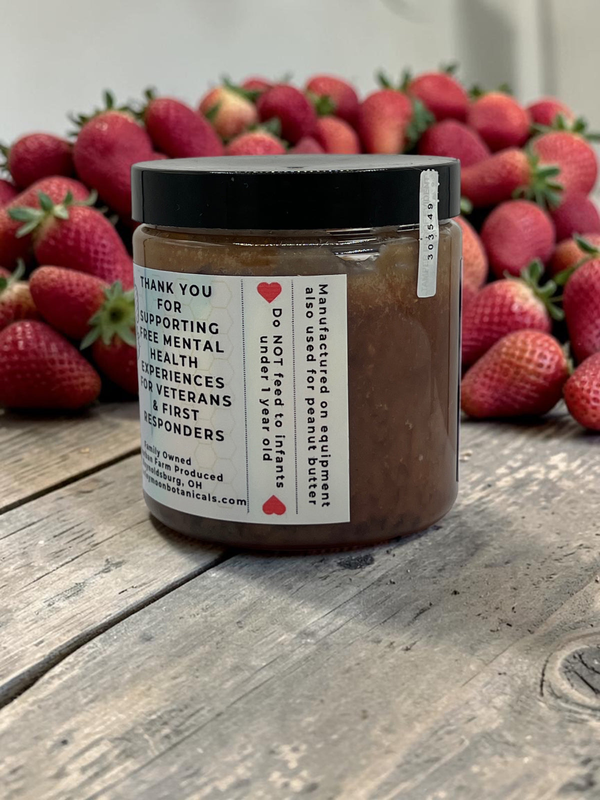 Barley Moon Botanicals Sweetie Berry strawberry creamed honey jar on a rustic wooden table with fresh strawberries.