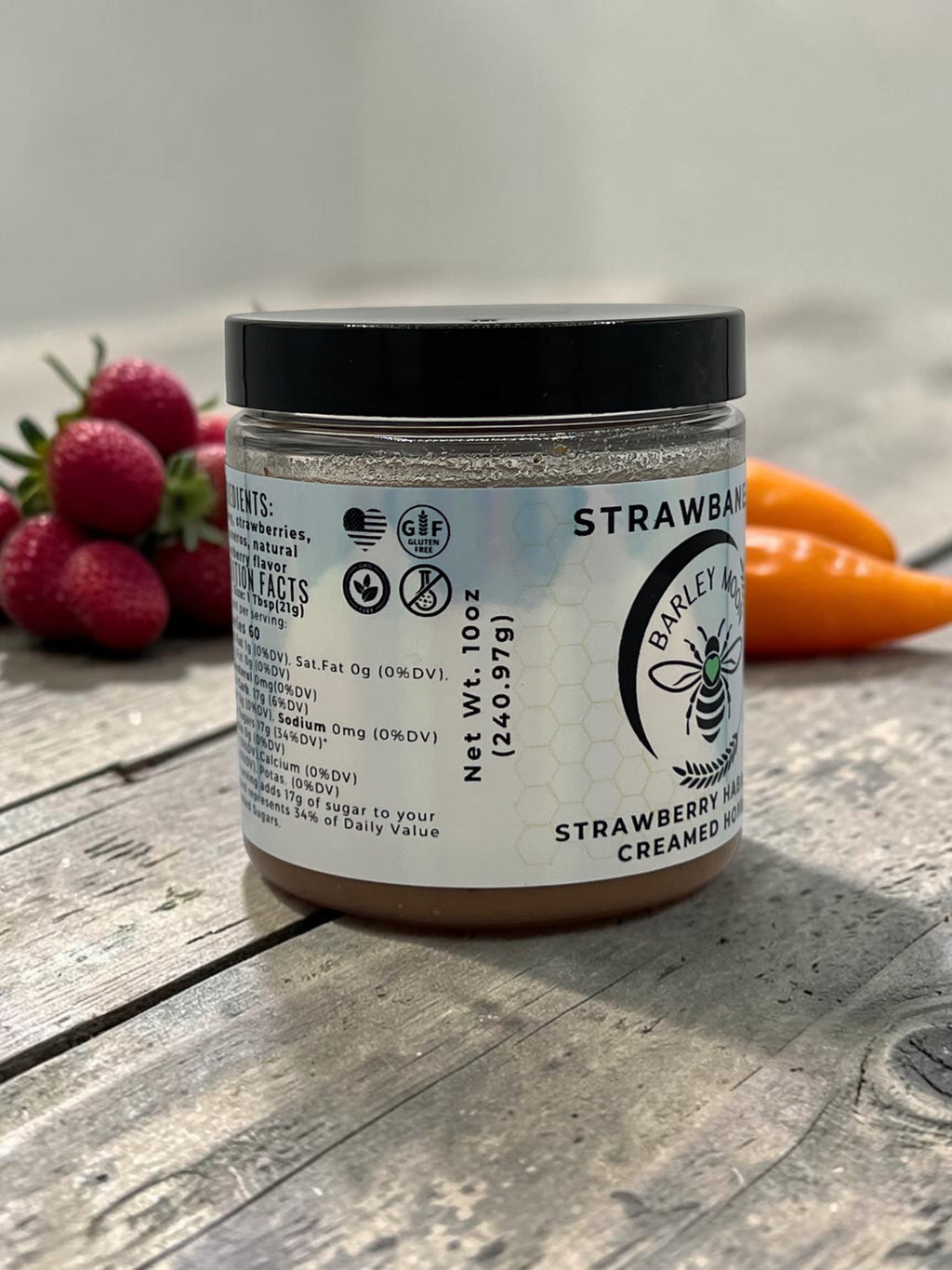 Barley Moon Botanicals Strawbanero creamed honey jar with strawberry and habanero pepper accents on a wooden surface.