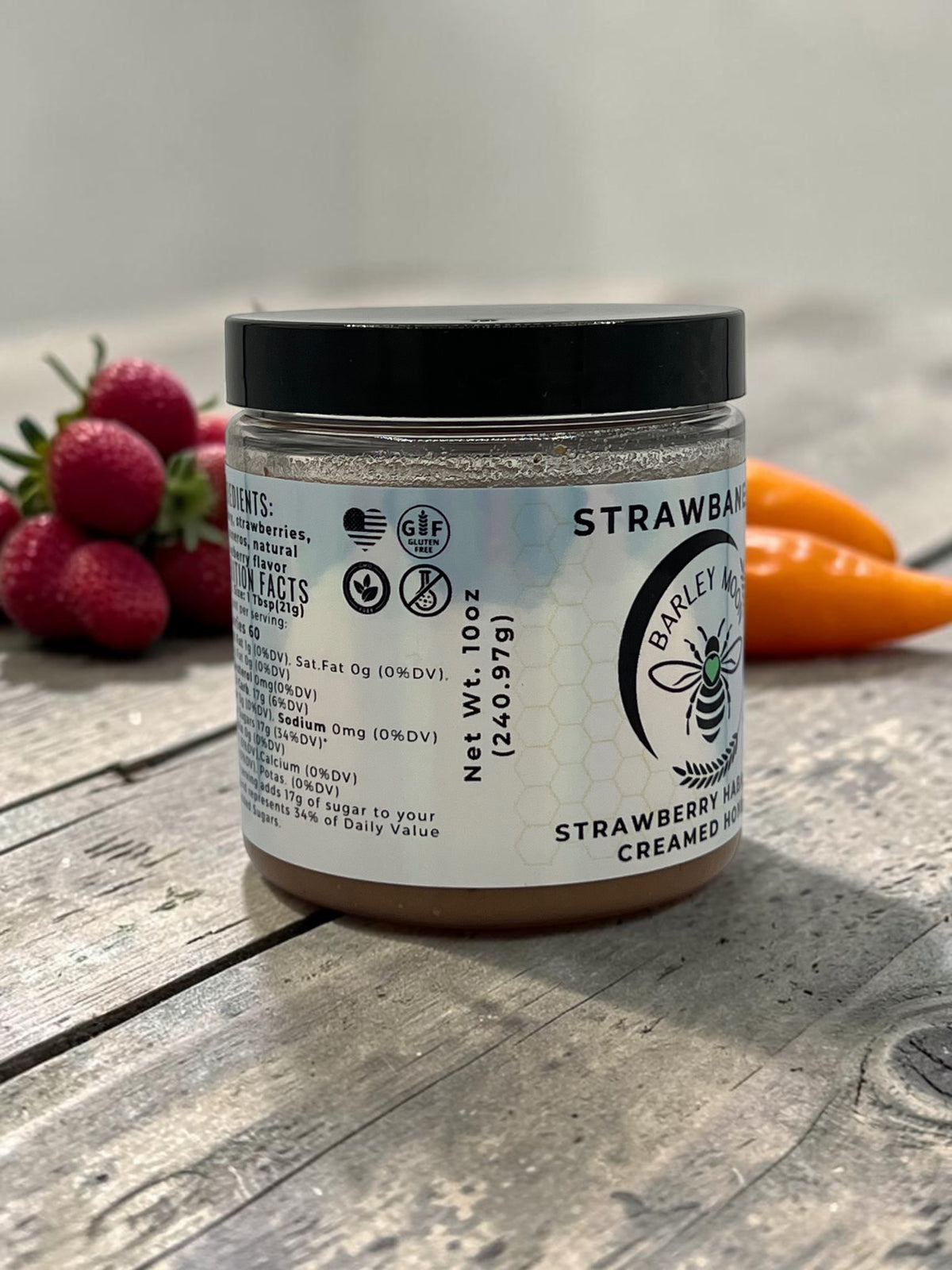 Barley Moon Botanicals Strawbanero creamed honey jar with strawberry and habanero pepper accents on a wooden surface.