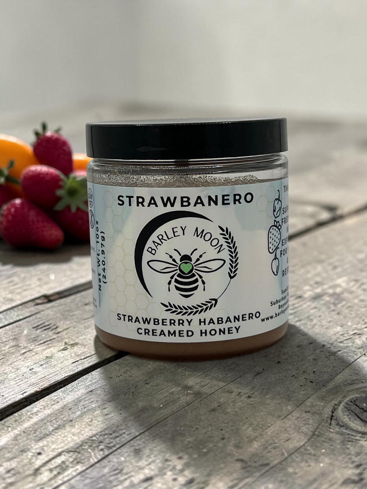Barley Moon Botanicals Strawbanero strawberry habanero creamed honey in a glass jar on a rustic wooden surface.