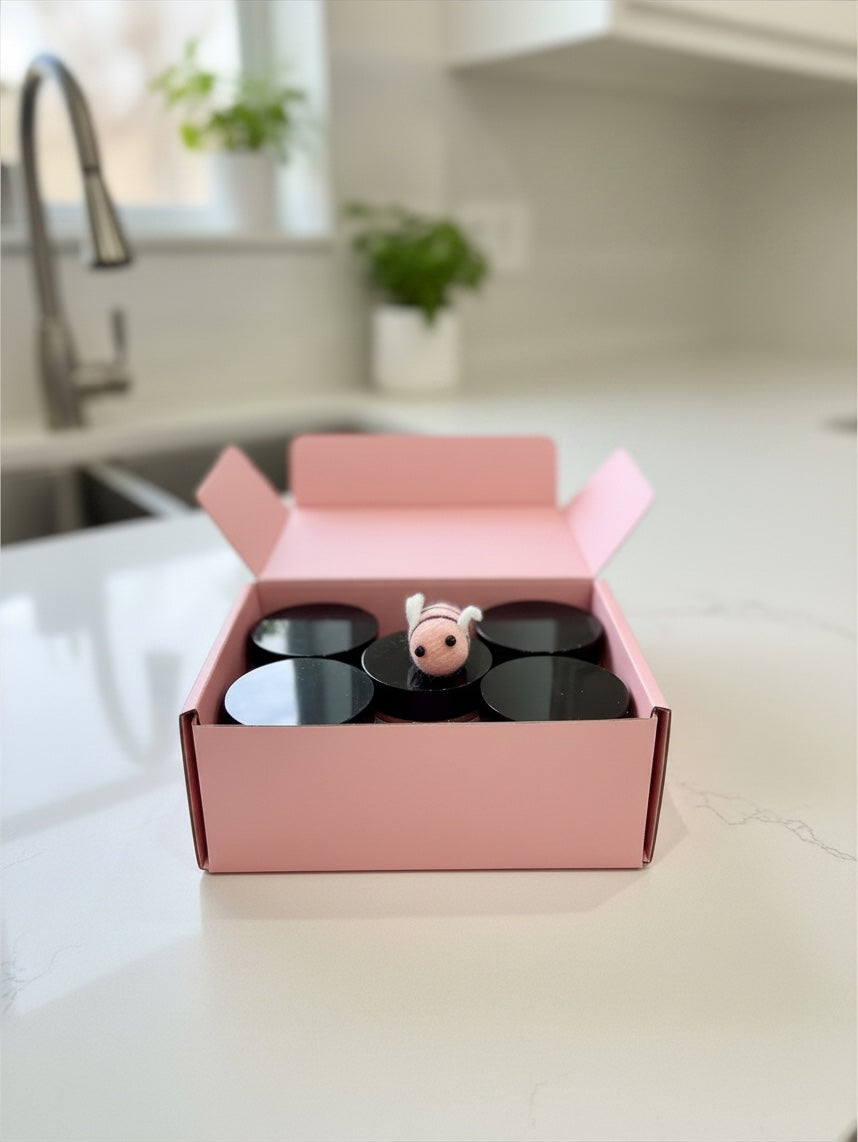Barley Moon Botanicals Bee Mine whipped honey flight in a pink gift box with a small felt bee on a kitchen counter.