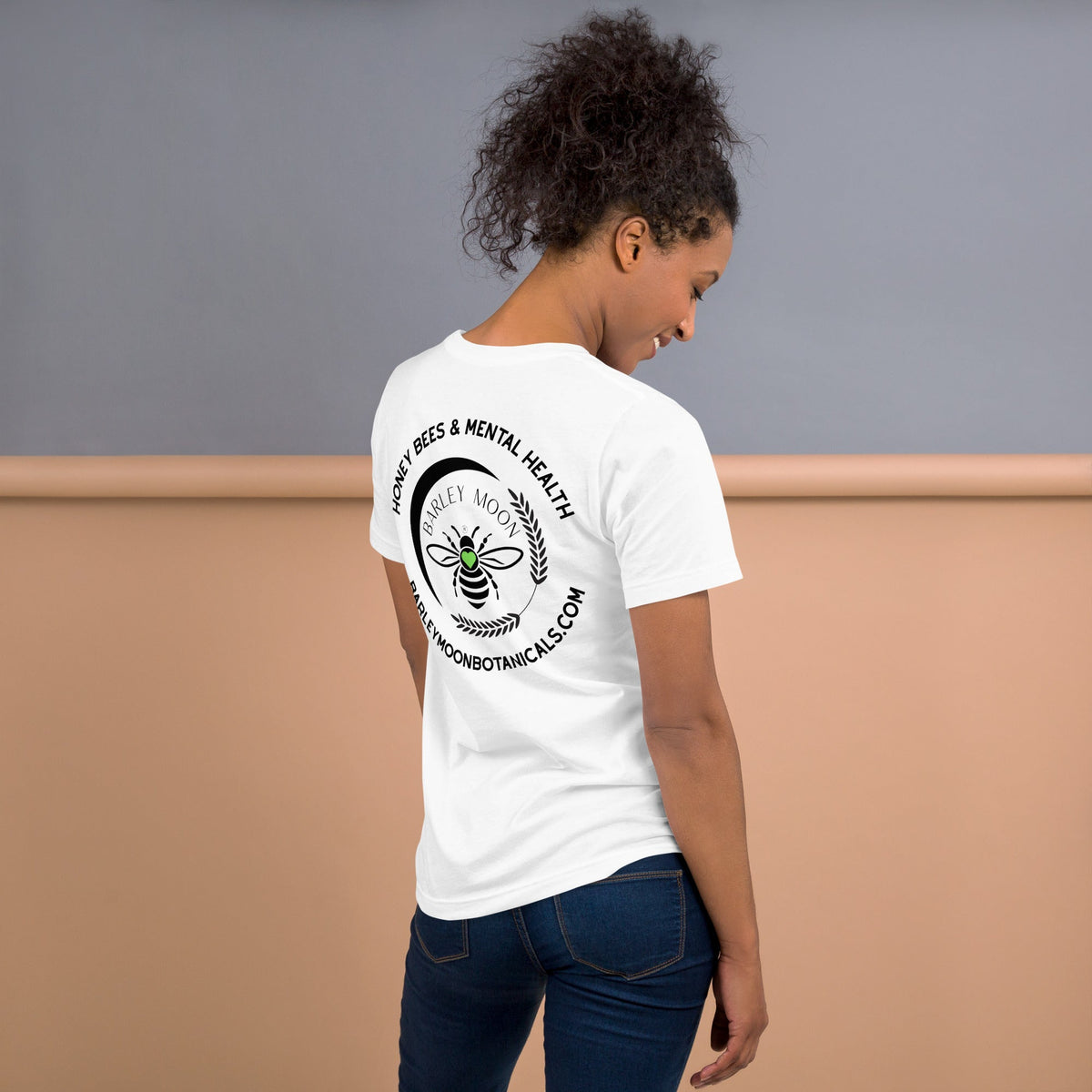 Woman wearing a white Barley Moon Botanicals t-shirt with a black bee and crescent moon logo on the back