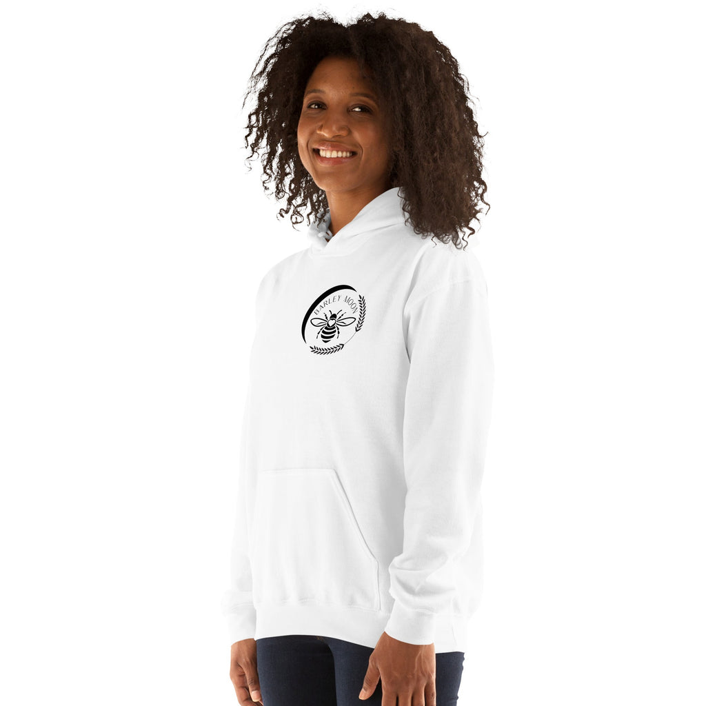 A woman wearing a white Barley Moon Botanicals unisex hoodie with a black bee and crescent moon logo on the chest.